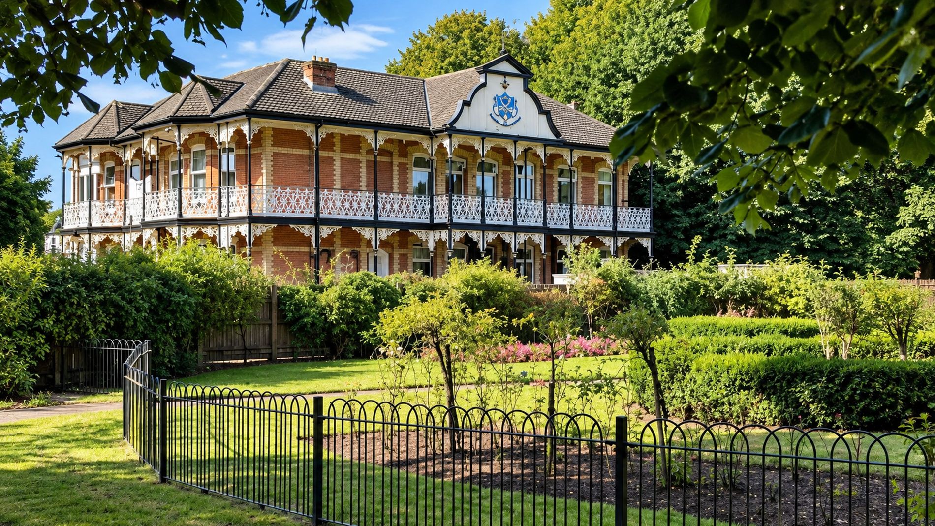Higher Park Lodge in summer, framed by trees, with its gardens and low hedges in front.